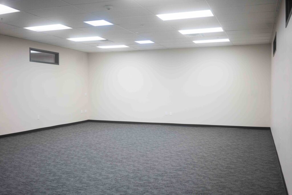 Empty renovated room with fresh gray carpet, painted walls, and a small high window