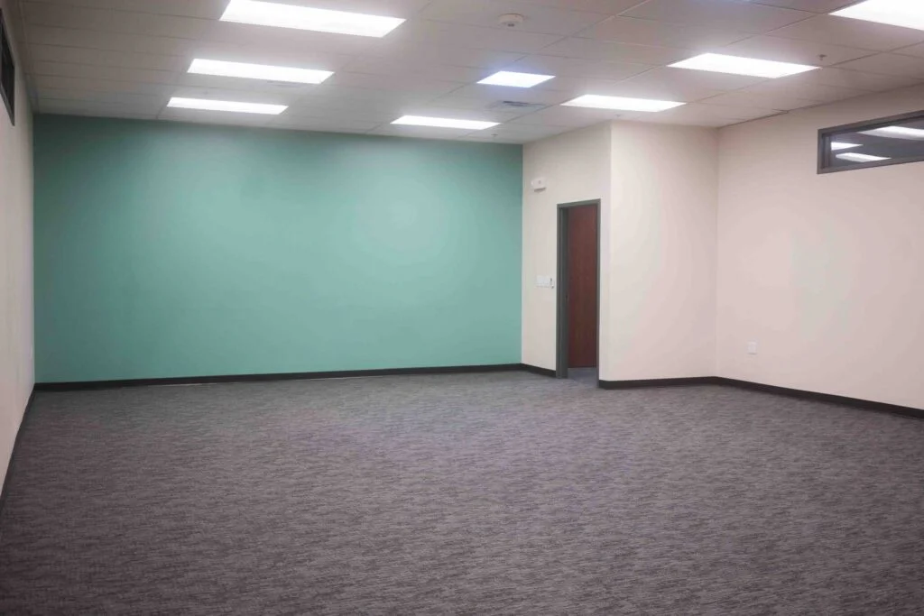 Empty finished room featuring a teal accent wall, wood door, and new carpet