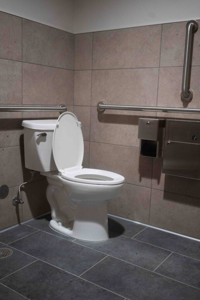 Wall-mounted toilet with stainless steel grab bars in a newly built accessible restroom