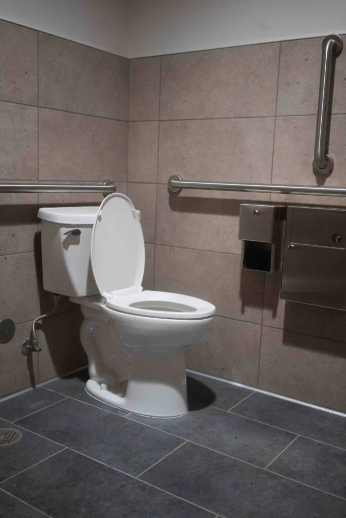 Wall-mounted toilet with stainless steel grab bars in a newly built accessible restroom