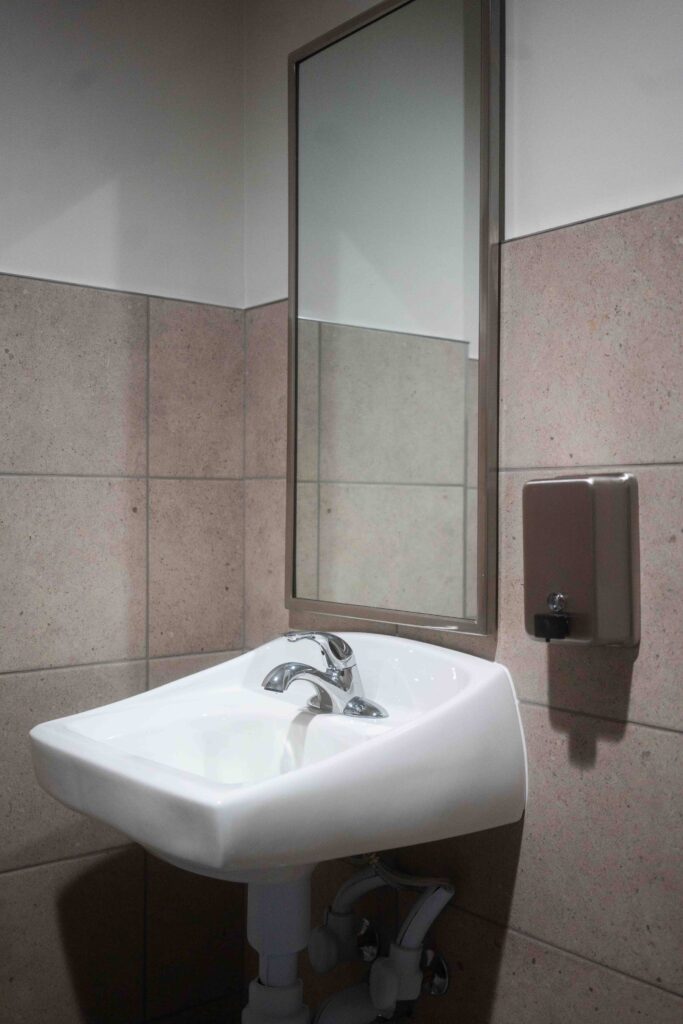 Wall-mounted ADA sink with mirror and soap dispenser in a tiled restroom