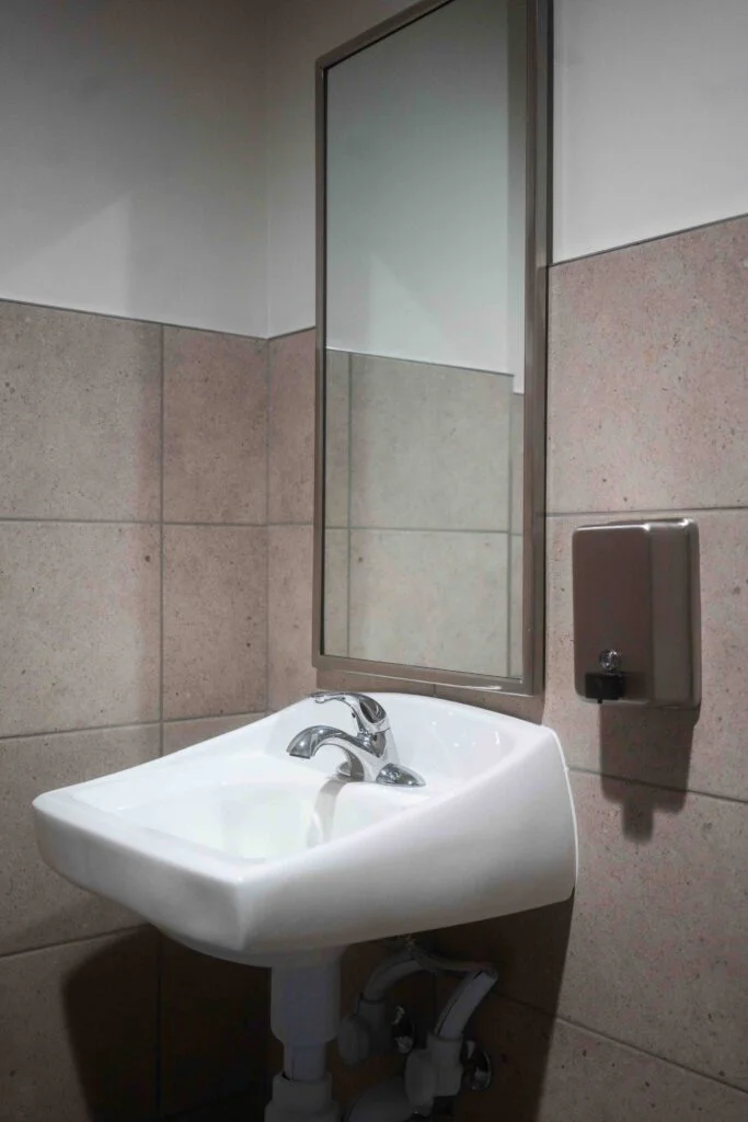 Wall-mounted ADA sink with mirror and soap dispenser in a tiled restroom