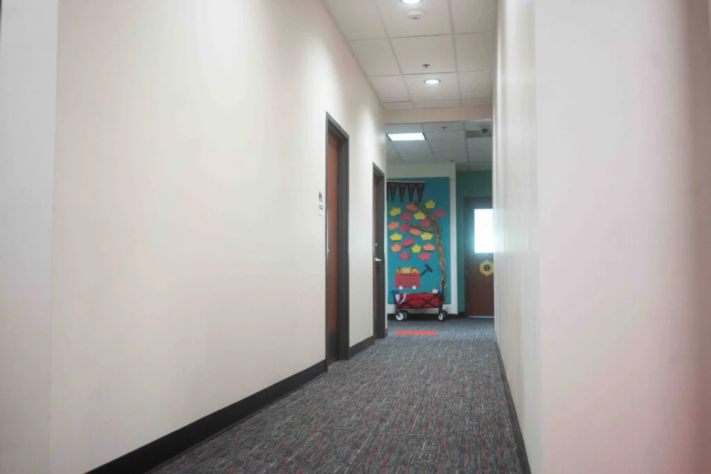 Hallway with red floor markings leading toward a classroom door decorated with pennants