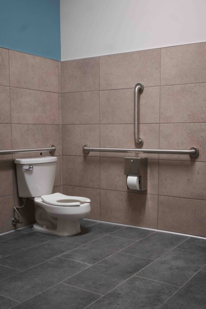 ADA toilet with grab bars and a teal-painted ceiling in a school restroom