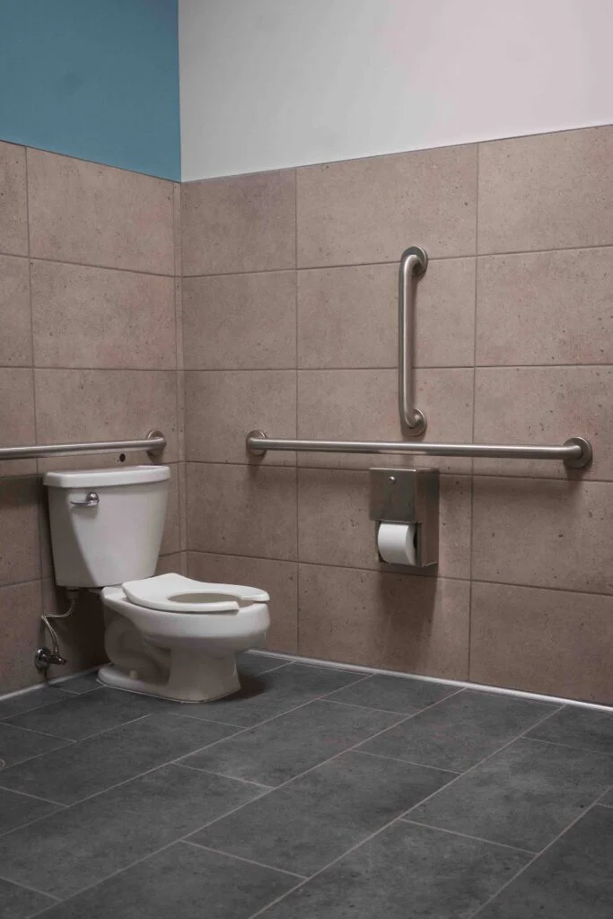 ADA toilet with grab bars and a teal-painted ceiling in a school restroom
