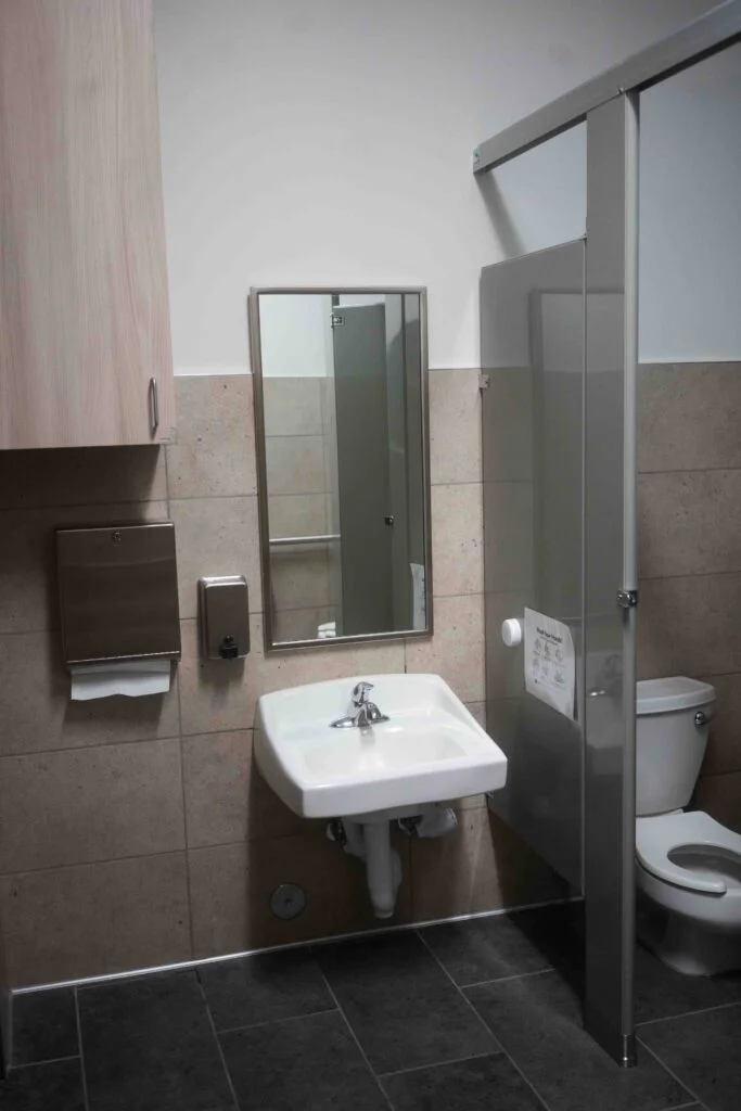Restroom sink and mirror beside an open stall door showing the toilet