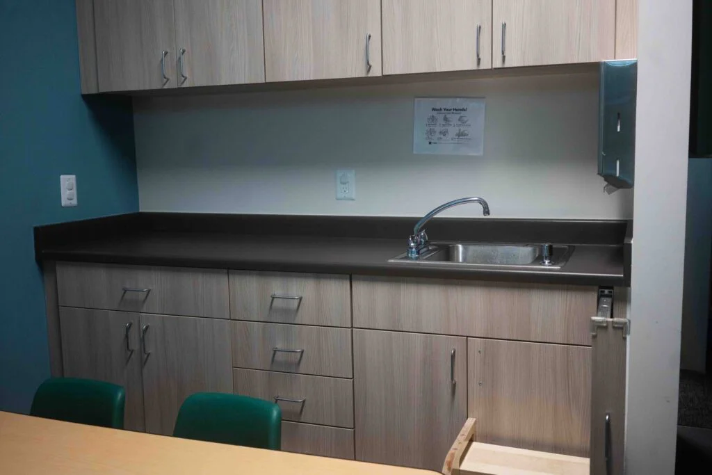 Classroom sink and countertop with wood cabinetry and a wash-your-hands sign