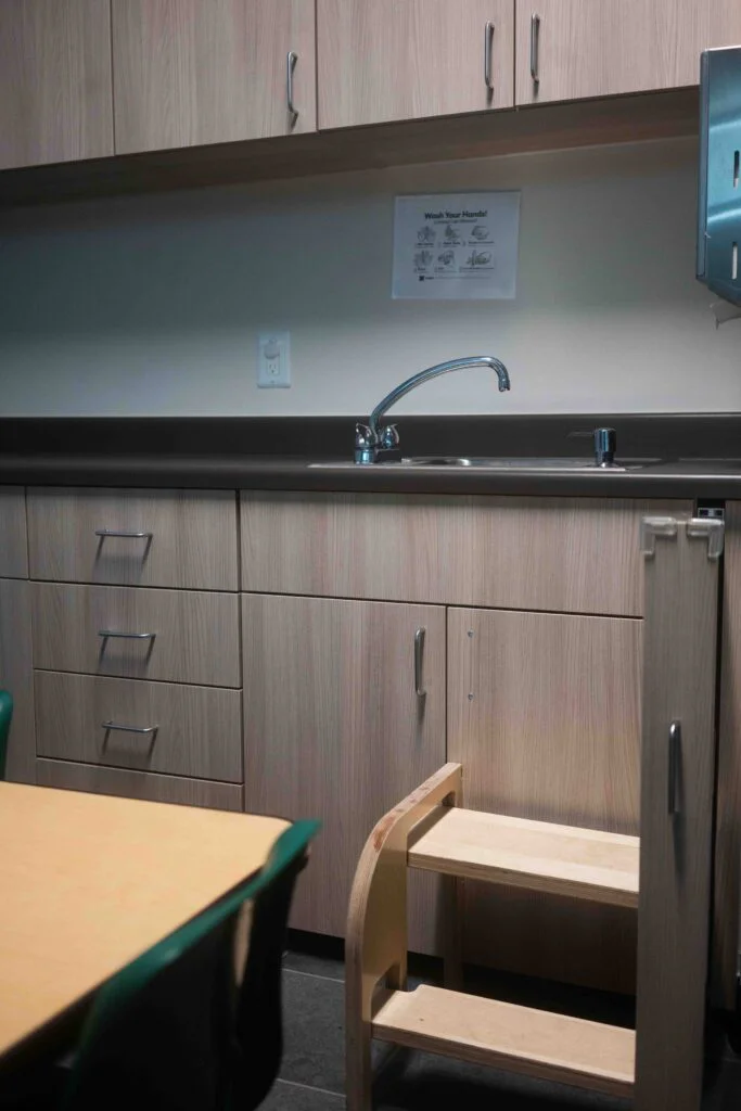 Wide view of a classroom sink, wood cabinetry, and paper towel dispenser