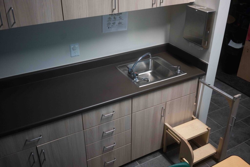 Classroom sink counter with wood-grain cabinetry and a nearby step stool