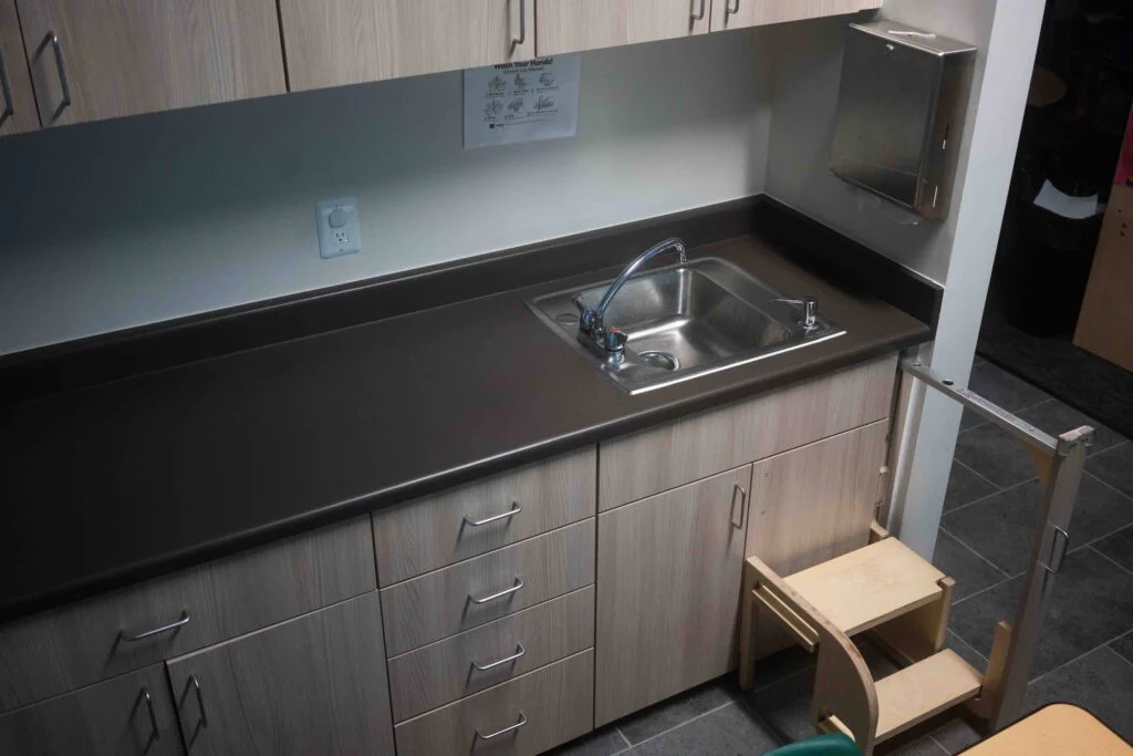 Classroom sink counter with wood-grain cabinetry and a nearby step stool