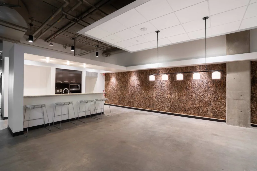 Kitchenette bar counter with stools facing a cork accent wall and pendant lighting