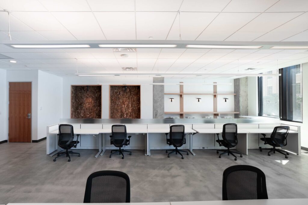 Open office desks with mesh task chairs beneath built-in wood shelving and cork-lined nooks