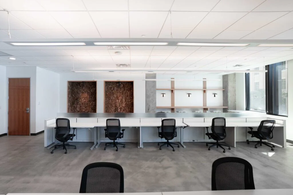 Open office desks with mesh task chairs beneath built-in wood shelving and cork-lined nooks