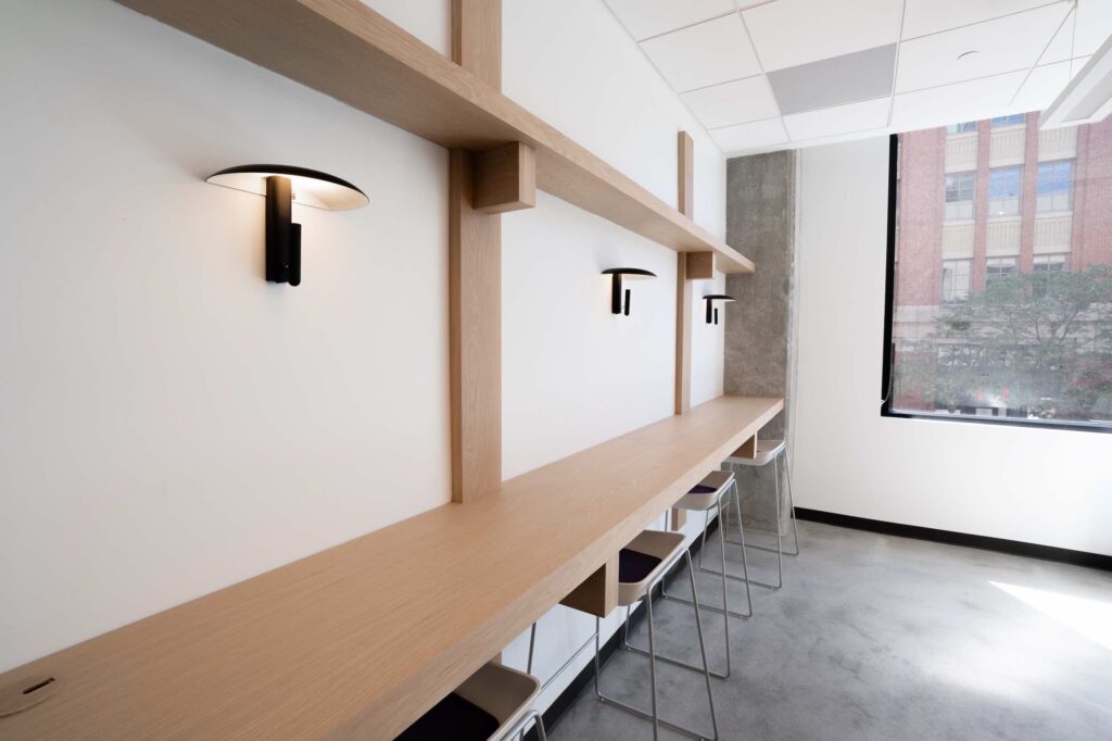 Wood shelf desk with stools, wall sconces and a city view window