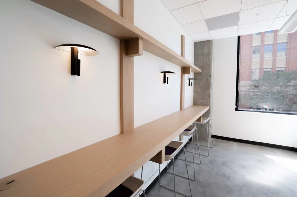 Wood shelf desk with stools, wall sconces and a city view window