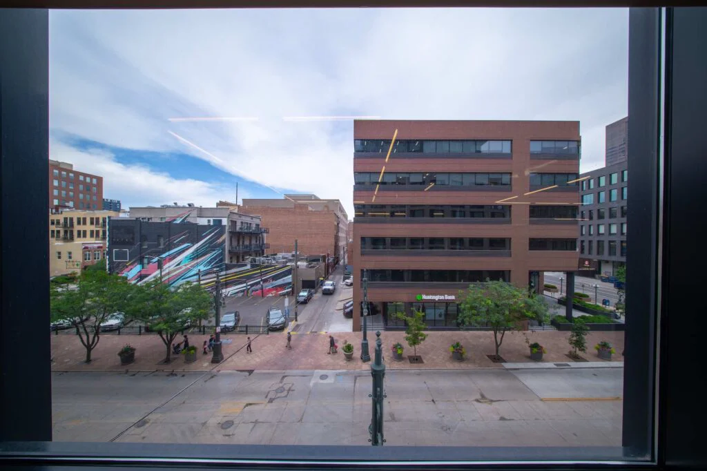 Window view of a downtown street with a brick office building, bank branch, and painted building mural below