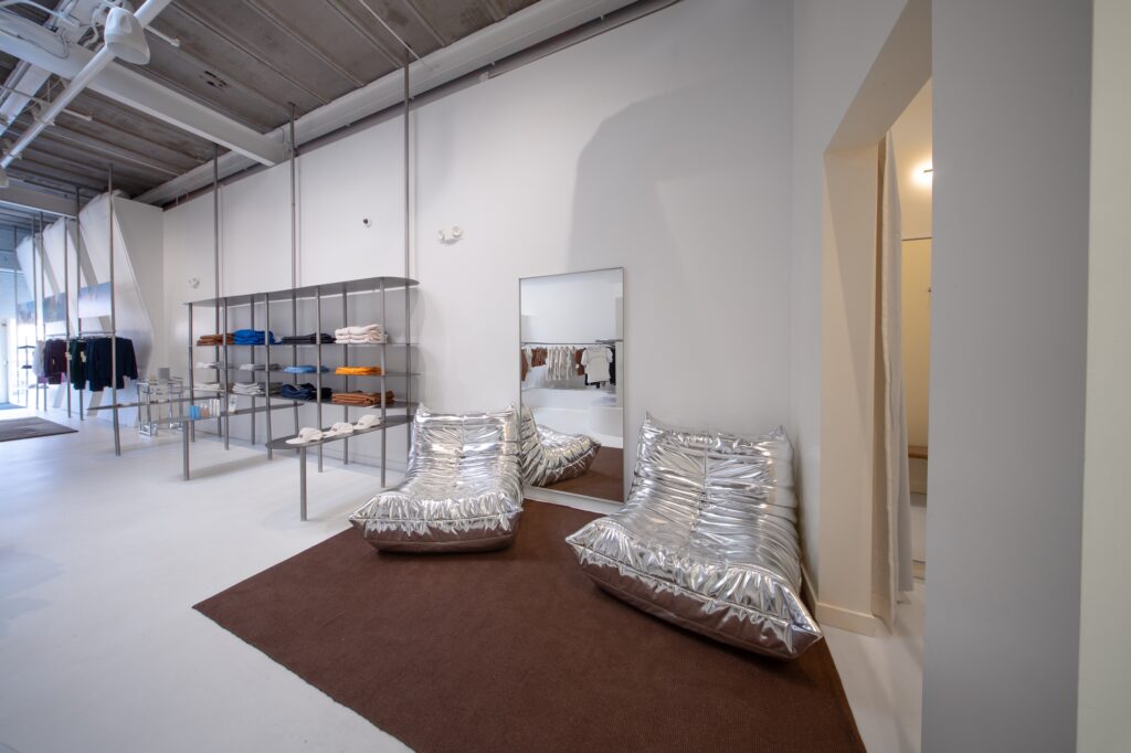 Retail store interior with metallic lounge chairs on a brown rug beside folded apparel shelving