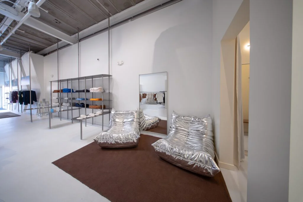 Retail store interior with metallic lounge chairs on a brown rug beside folded apparel shelving