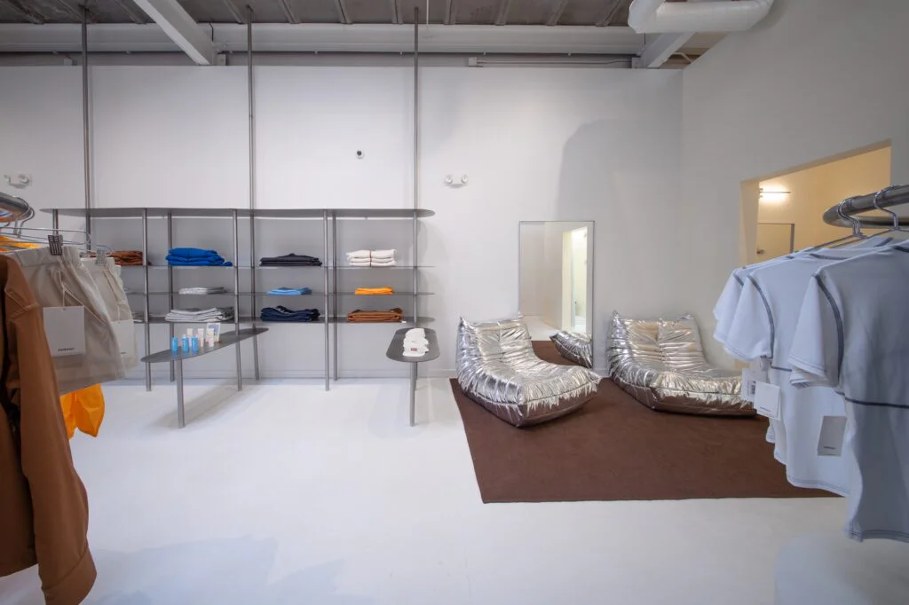 Clothing racks and folded apparel shelving next to metallic lounge chairs in a retail store