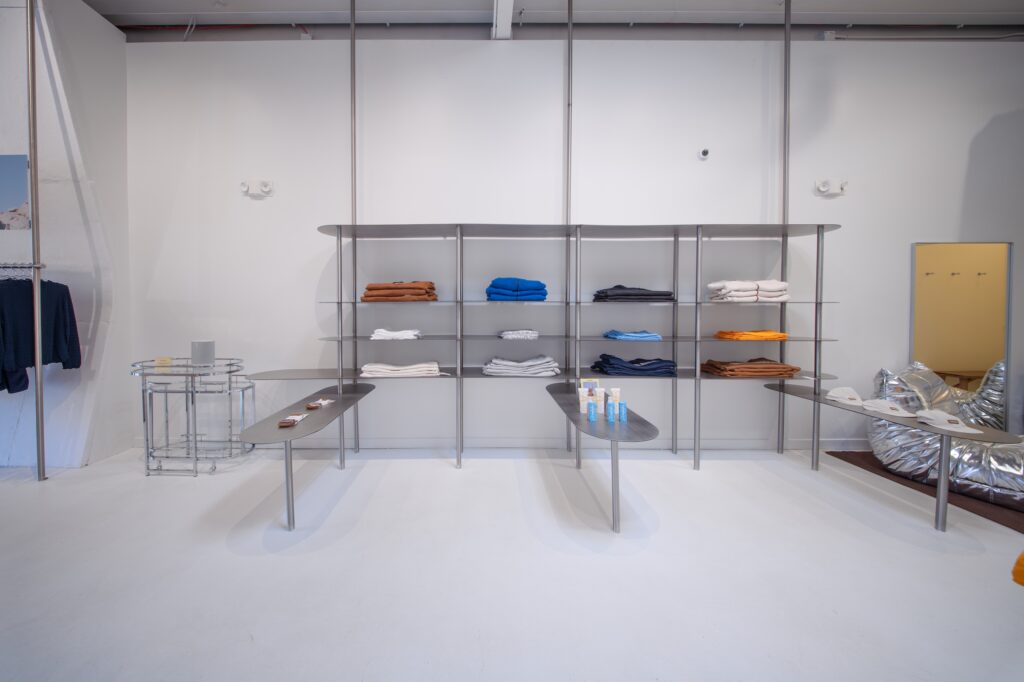 Steel shelving unit displaying folded clothing beside a mirror and rolling bar cart in a retail store