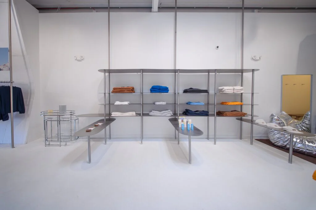 Steel shelving unit displaying folded clothing beside a mirror and rolling bar cart in a retail store