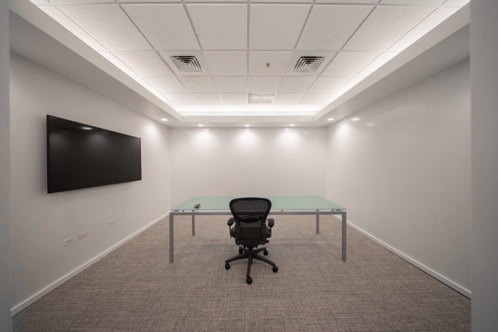 Conference room with a glass-top table, ergonomic office chair, and wall-mounted display screen