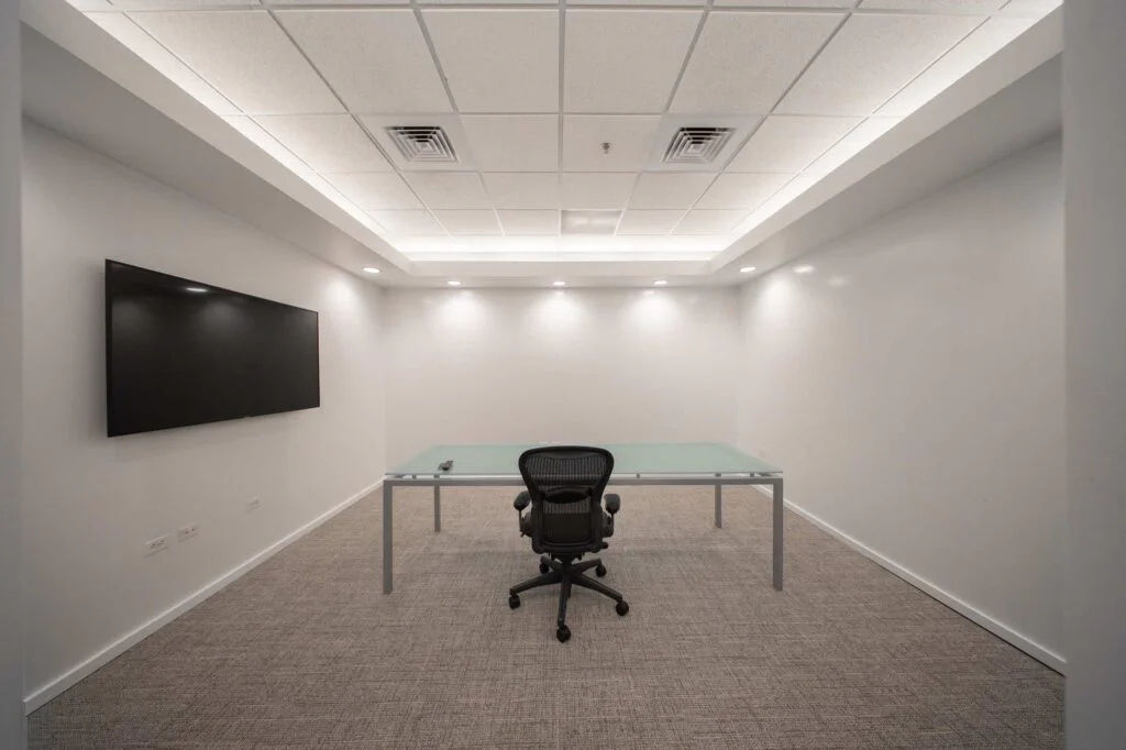 Conference room with a glass-top table, ergonomic office chair, and wall-mounted display screen