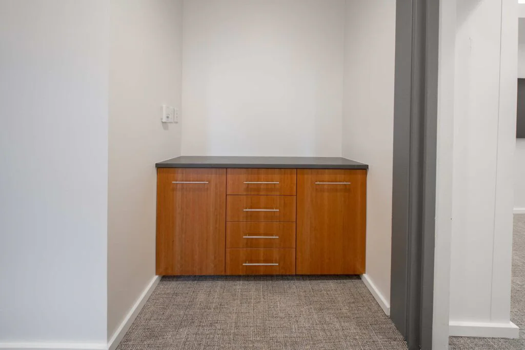 Built-in wood veneer credenza with dark countertop in a carpeted office alcove near a wall-mounted thermostat