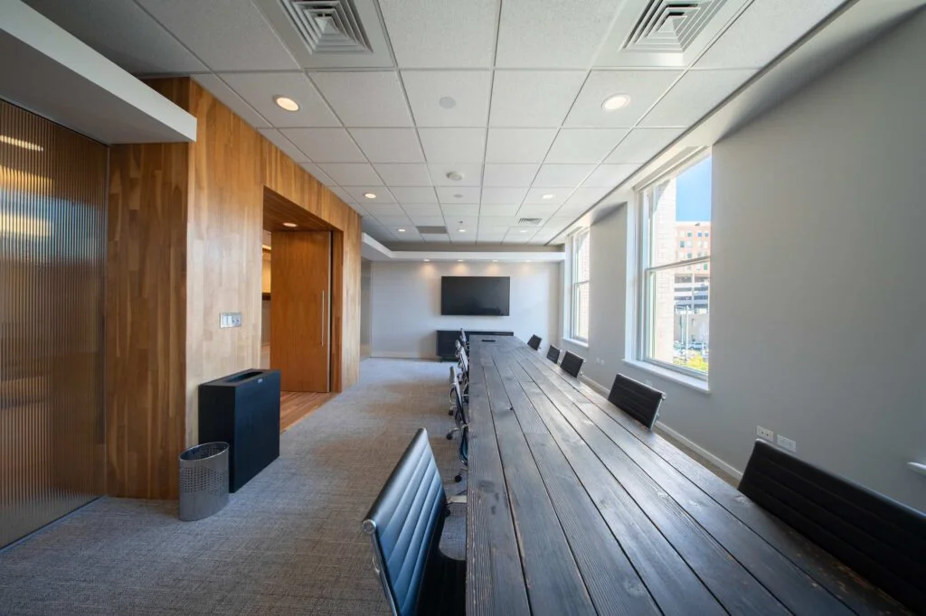Conference room with a rustic reclaimed wood plank table, black chairs, and a wood-clad entry with frosted glass walls