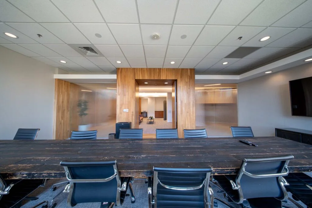 Dark wood conference table viewed through a wood-framed doorway that opens into the reception lounge beyond