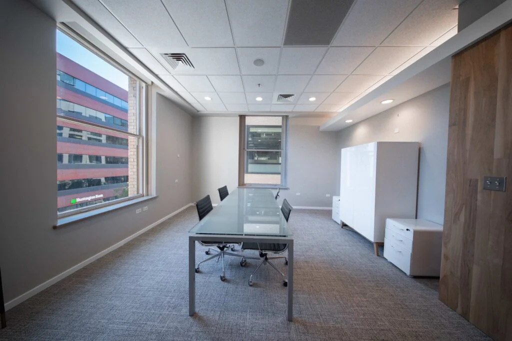 Small meeting room with a frosted glass table, black chairs, and floor-to-ceiling windows overlooking downtown