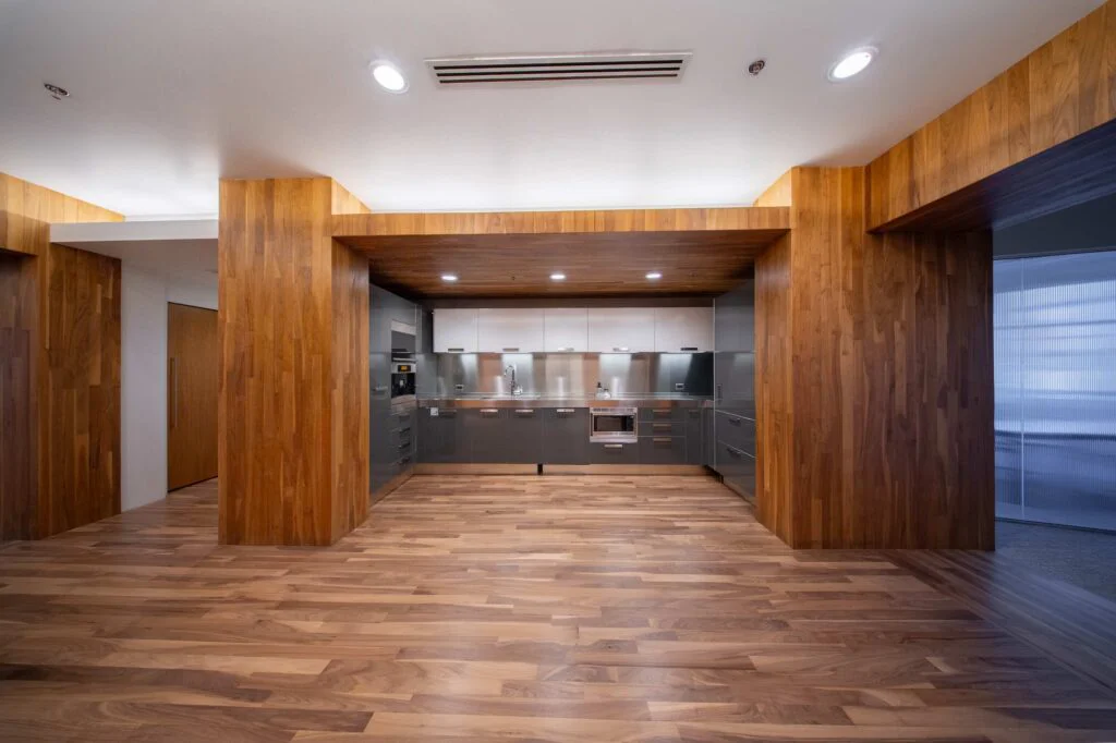Break room kitchen with graphite gray cabinets, stainless backsplash, and a wood-clad ceiling over walnut flooring