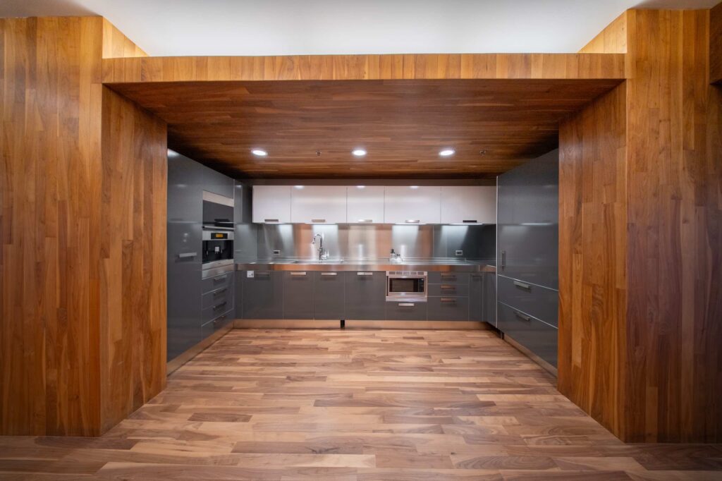 Close view of a break room kitchen with gray cabinets, built-in oven and microwave, and a wood-paneled overhead surround