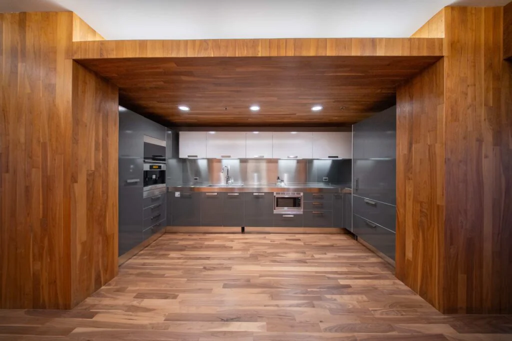 Close view of a break room kitchen with gray cabinets, built-in oven and microwave, and a wood-paneled overhead surround
