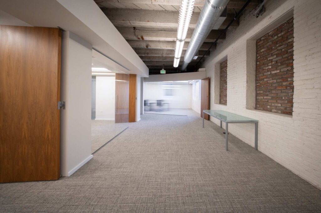 Interior hallway with a painted brick wall, an open solid wood door, and a glass-walled meeting room beyond