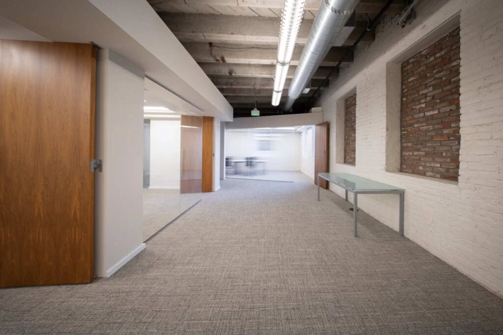 Interior hallway with a painted brick wall, an open solid wood door, and a glass-walled meeting room beyond