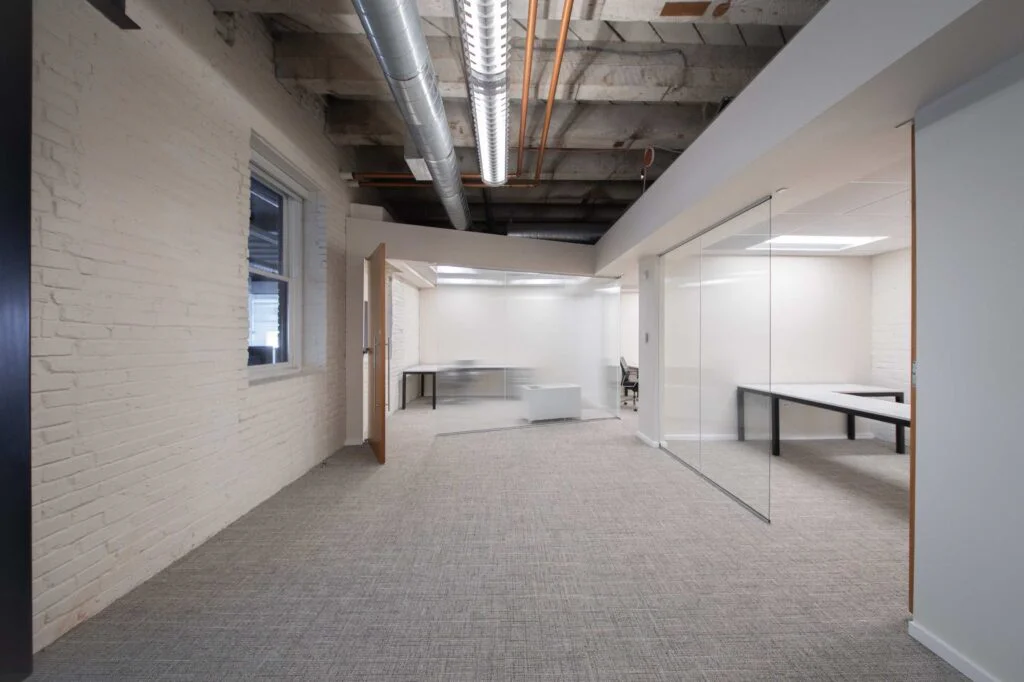 Office hallway with an exposed painted brick wall, a window view of neighboring buildings, and an open wood door