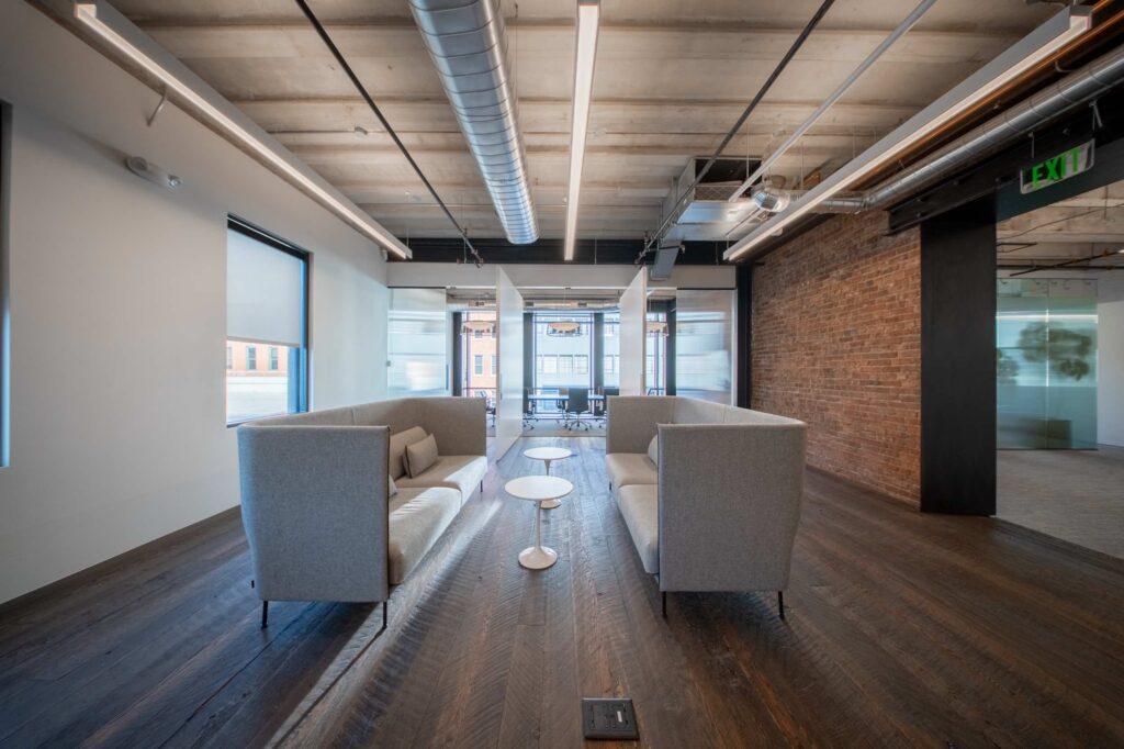 Casual lounge with two gray high-back sofas facing each other on wood flooring beside an exposed brick wall
