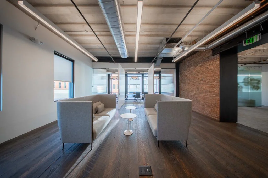 Casual lounge with two gray high-back sofas facing each other on wood flooring beside an exposed brick wall
