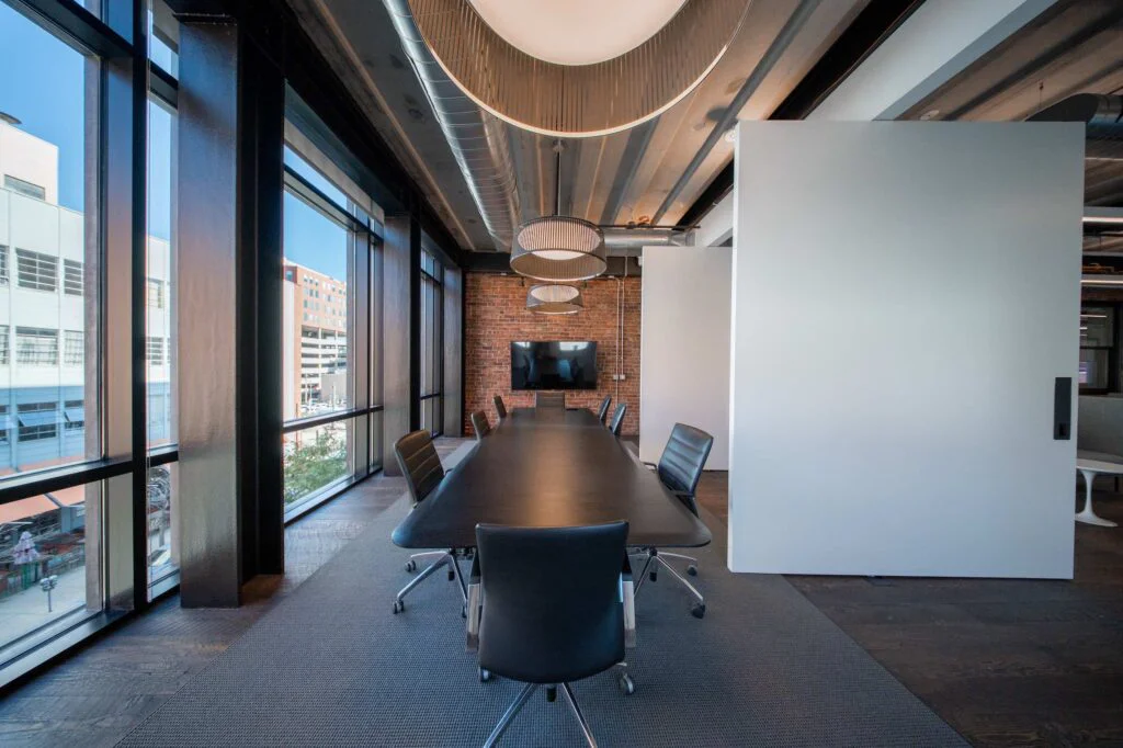Corner conference room with black pendant lights, an exposed brick wall, a TV, and floor-to-ceiling city windows