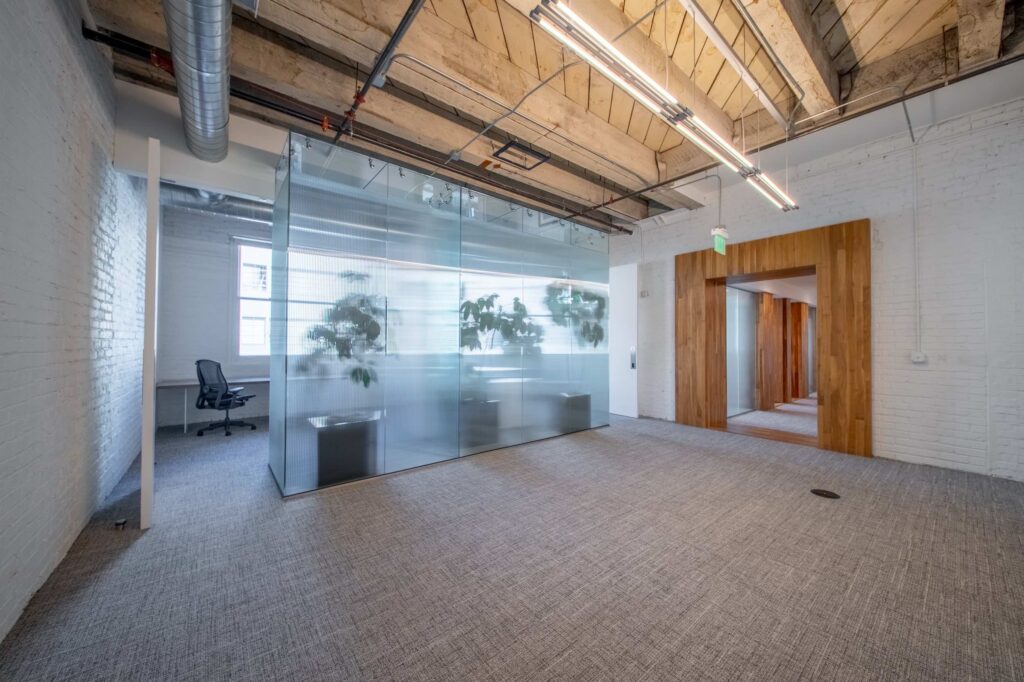 Frosted glass-enclosed office filled with greenery, flanked by white doors and an exposed brick wall