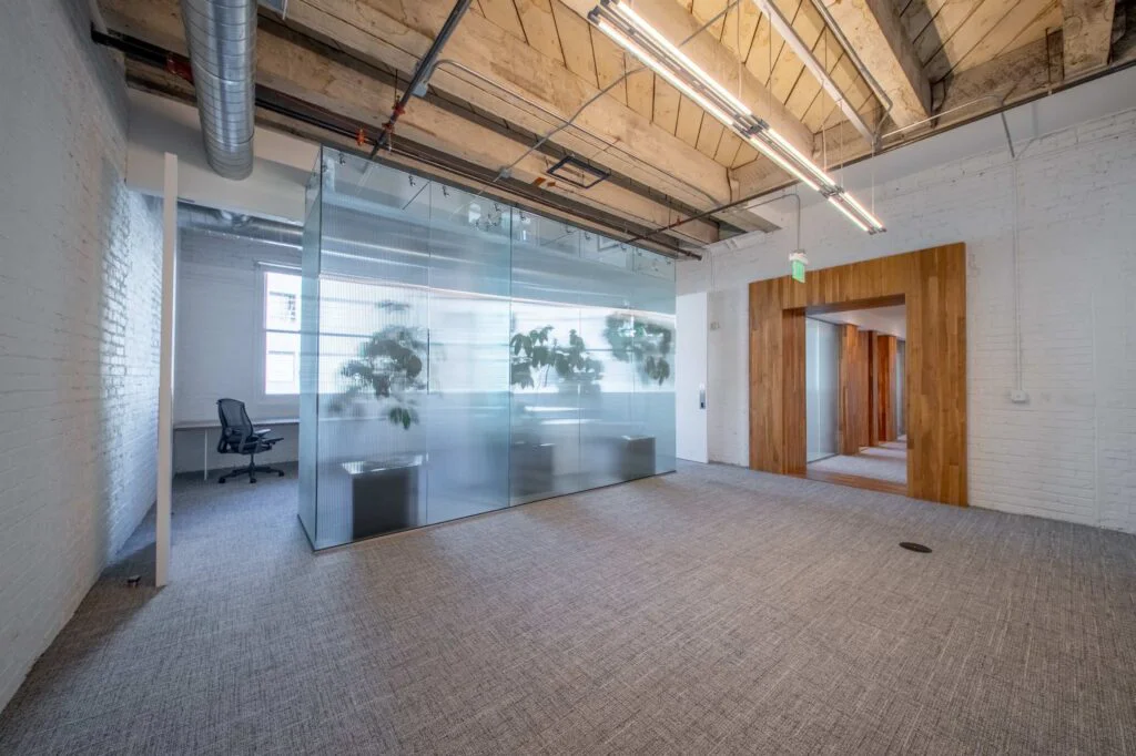 Frosted glass-enclosed office filled with greenery, flanked by white doors and an exposed brick wall
