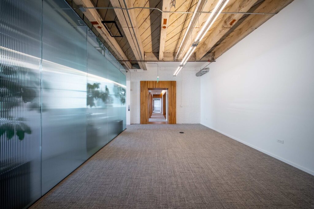 Long hallway with a frosted glass partition wall on one side and a wood-framed doorway further down the corridor