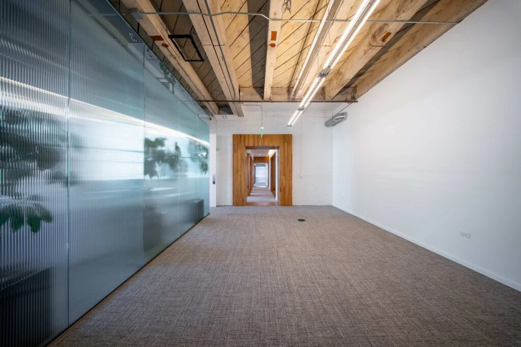 Long hallway with a frosted glass partition wall on one side and a wood-framed doorway further down the corridor