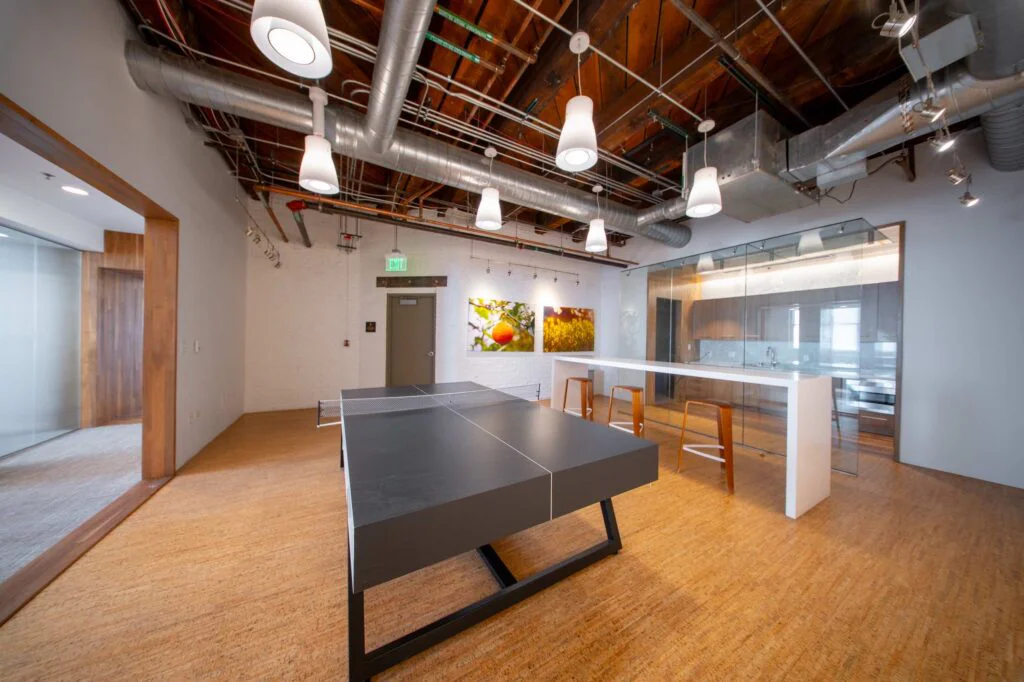 Ping pong table and high-top bar seating in an open recreation space that connects to the glass-enclosed kitchen