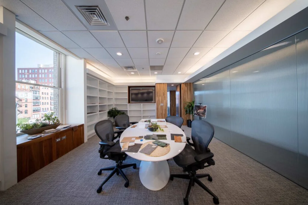 Design studio with built-in white shelving for material samples, a round table, and a wall-mounted display screen