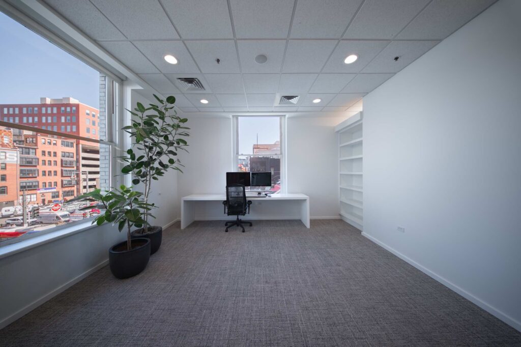 Private office with a white desk, dual monitors, built-in bookshelves, and windows overlooking downtown rooftops