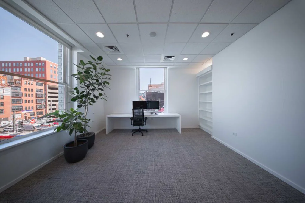 Private office with a white desk, dual monitors, built-in bookshelves, and windows overlooking downtown rooftops