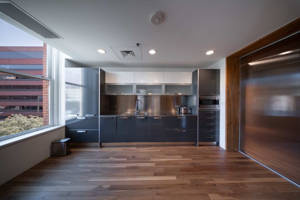 Office kitchen with dark gray cabinetry, stainless steel backsplash and countertop, and wood flooring