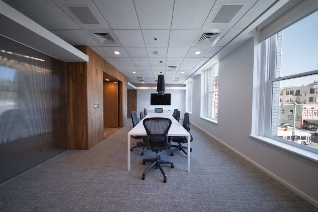 Long conference table and mesh chairs in a wood-paneled meeting room with floor-to-ceiling windows overlooking downtown street